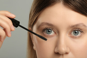 Woman applying mascara onto eyelashes against grey background, closeup