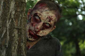 Scary zombie near tree outdoors. Halloween monster