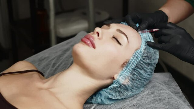 Face woman getting beauty injection in cosmetic clinic. Close up cosmetologist doing botox injection in forehead to patient in beauty clinic. Rejuvenation, injectable cosmetology and medicine concept