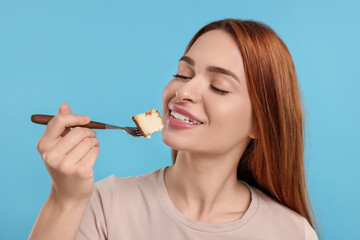Obraz premium Young woman eating piece of tasty cake on light blue background
