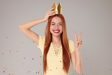 Beautiful young woman with princess crown under falling confetti on light grey background