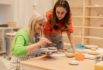 teacher helping senior student in a ceramics workshop for retirees - obrazy, fototapety, plakaty