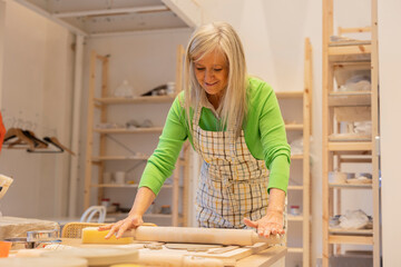 senior woman with gray hair rolling clay with roller