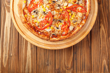 delicious pizza with chicken, mushrooms, cheese, tomatoes and corn on a wooden background