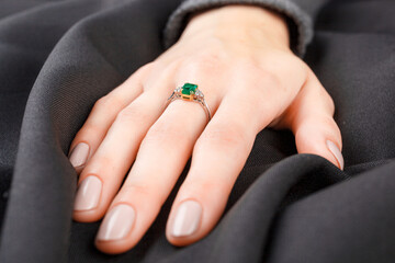 Beautiful female hand with gold ring with diamonds and emerald on gray background - obrazy, fototapety, plakaty