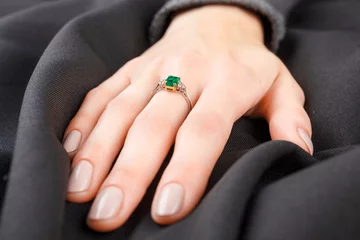 Poster Beautiful female hand with gold ring with diamonds and emerald on gray background © Minakryn Ruslan 