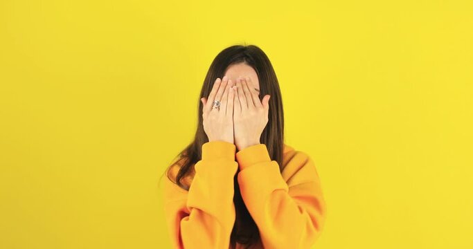 Woman covers hands with palms, hides face, plays hide and seek. Confused excited woman open face looking at camera with big eyes in surprise, shocked. Oh my god wow. Peekaboo isolated on yellow wall.