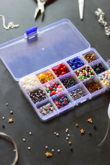 Box with colorful beads, string, wire, chain, scissors, pliers and hammer on dark background. Various jewelry making supplies. Selective focus.