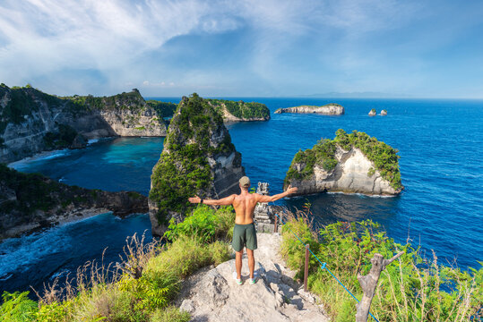 Rear view of a young man with outstretched arms standing on top of a cliff overlooking the ocean, Diamond beach, Nusa Penida, Klungkung regency, Bali, Indonesia, Southeast Asia