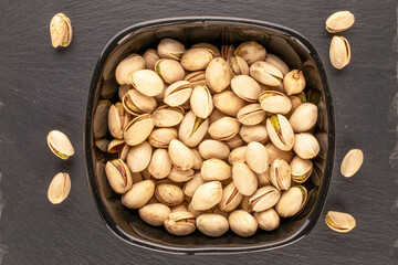 A few tasty pistachios in a black ceramic plate on a slate stone, macro, top view.