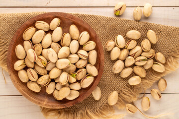 A small amount of delicious pistachios in a wooden plate with a jute napkin on a wooden table,...