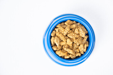 A treat for cats and kittens is a fish-shaped catnip cookie in a blue bowl, copy space for text.