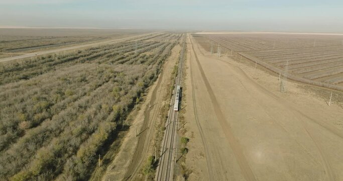 Passenger train an electric locomotive by two sided straight railway arid flat steppe - Aerial drone view at autumn sunny day