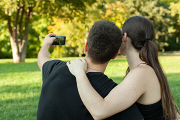 Pareja haciendose un selfie en el cesped del parque. Espalda de un selfie