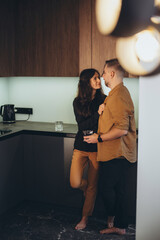 Young couple in the kitchen. The girl holds the guy by the shirt. The man holds a glass of water in his hand and looks at the girl.