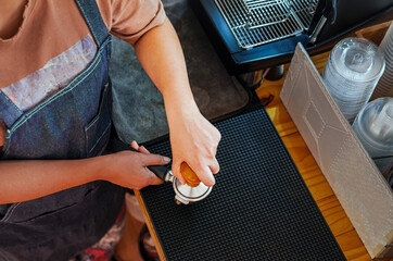 Top view of barista holding portafilter and coffee tamper making an espresso coffee in coffee shop