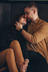 A young couple sits barefoot on the kitchen floor. The girl, smiling, threw her legs over the guy and pressed herself into his eyes. A guy touches a girl's face with his hand