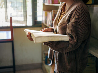 Learning, education Hand of Senior woman standing holding a book in library by the window in the morning, relax and enjoy books.