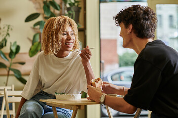 happy african american woman with braces eating salad bowl near blurred boyfriend in vegan cafe - obrazy, fototapety, plakaty