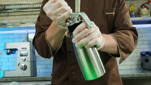 Chef screws in and locks in new carbon dioxide charger. Man uses whipping siphon for further carbonation of high-fat cream