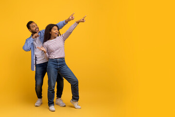 Check This. Happy black couple pointing at copy space on yellow background