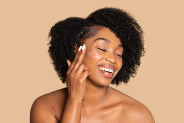 Joyous woman applying moisturizer on cheek, beauty routine