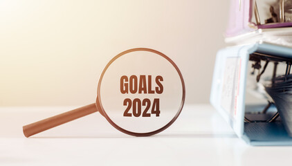 Focused on business concept. Magnifying glass with message GOALS 2024 on an office background. Search new goals for business