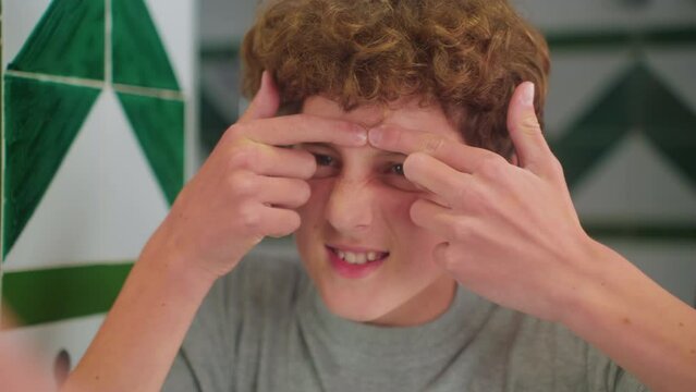 Cute teenager with curly hair crushes pimples in the bathroom. Concept awkward age, problems with the skin, hormonal background, difficulties of teenagers. Close up