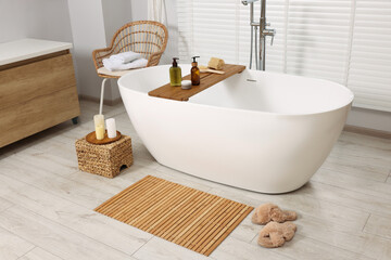 Stylish bathroom interior with bamboo bath mat and white tub