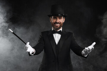 Happy magician holding wand in smoke on black background