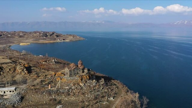 Medieval stone monastery on the shore of Lake Sevan. Aerial view church in Armenia. Drone fly above Ancient church, monastery․ Tourists near monastery. Famous touristic place.