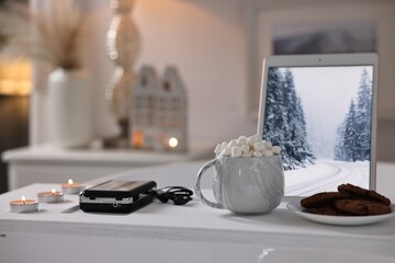 White wooden tray with tablet, cassette player, hot drink and burning candles on bathtub in bathroom