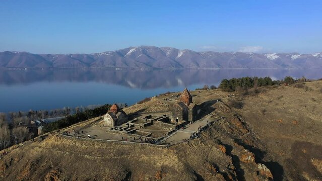 Medieval stone monastery on the shore of Lake Sevan. Aerial view church in Armenia. Drone fly above Ancient church, monastery․ Tourists near monastery. Famous touristic place.