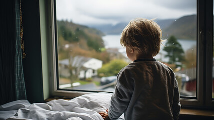 Fototapeta premium Back view of kid patient sitting on hospital bed looking out of window. Preteen sick boy sitting on bed in hospital ward.