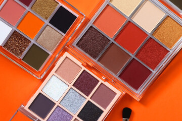 Colorful eyeshadow palettes and make up brush on orange background. Top view.