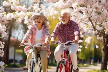 Fotobehang Youthful and playful happy senior old couple enjoy outdoor leisure activity riding bikes in spring cherry blossom park. Elderly Man woman in healthy active lifestyle. Retired people using bicycle © m