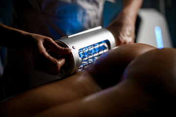 Female hands of a beautician are performing an anti-cellulite massage with device on the buttocks...