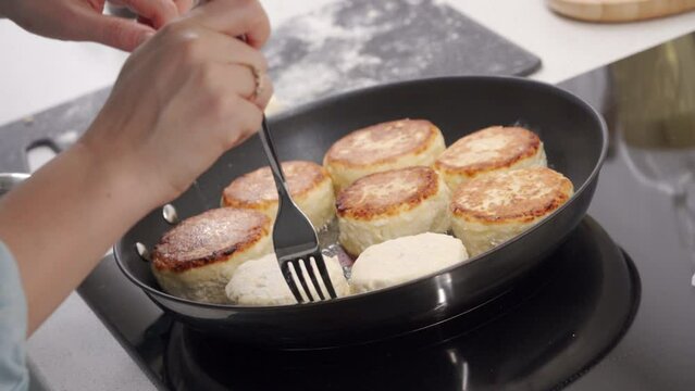 Cooking fried quark pancakes Syrniki. Pancakes are fried in a frying pan. Belarusian, Russian, Ukrainian cuisine.