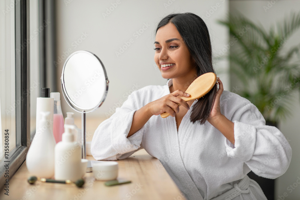 Wall mural cheerful indian woman combing beautiful dark long hair at bathroom