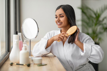 Cheerful indian woman combing beautiful dark long hair at bathroom