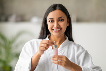 Smiling Young Indian Woman Applying Face Serum With Dropper