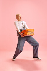 Full length portrait of young attractive woman in denim overall carrying huge stack of boxes with...