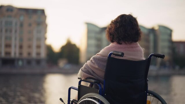 Woman in wheelchair walking in city. Senior mature woman breathing air outdoor thinking looking around enjoying pastime in evening. Live with physical disability, special needs people concept.