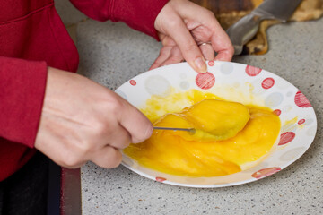 Woman's hands with a fork mixing eggs in a plate to prepare them.