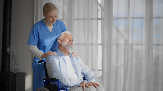 Nurse massaging neck to paralyzed man. Senior male in wheelchair enjoying massage in clinic. Social medical worker provides care support help. Living with legs paralysis, special needs people concept.