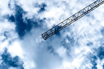 fragment of a construction crane against a blue sky with white c