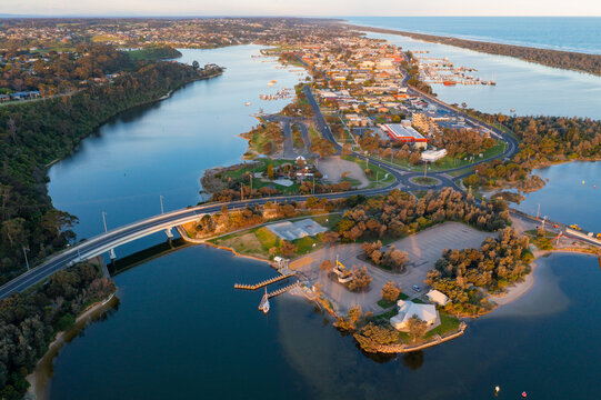 Aerial view of a curved road bridge over a river joining a forest area and a coastal town
