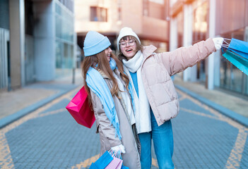 women girlfriends with colorful shopping gift bags having a fun time together, talking and using phones outdoor in urban city. people, communication, friendship, shopping and lifestyle concepts