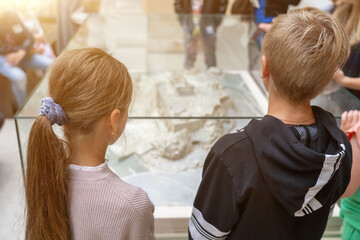 Two children look at a model of an ancient building on display in a museum.