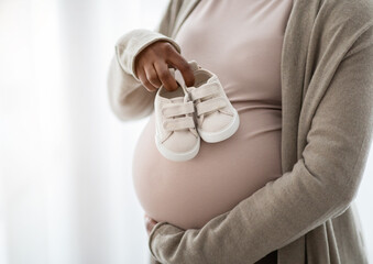 Cropped of pregnant woman holding small baby shoes, window background
